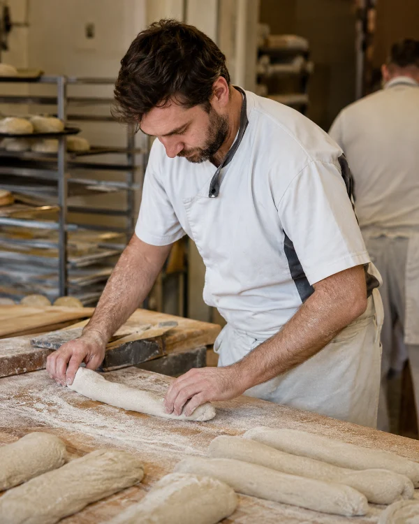 Un boulanger façonne des pâtons de baguette au fournil